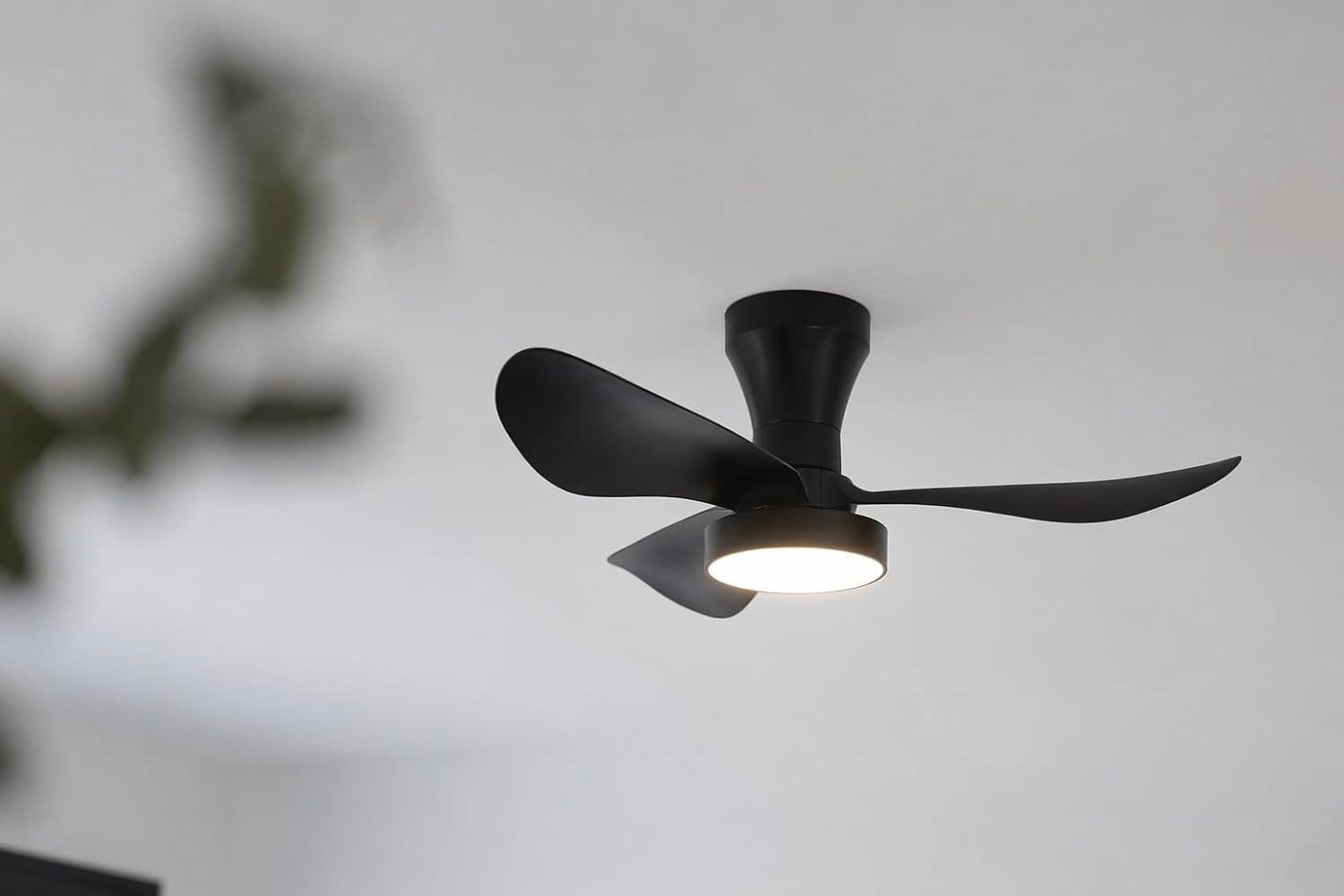 Un ventilador de techo negro moderno con tres aspas y luz está montado en un techo blanco.