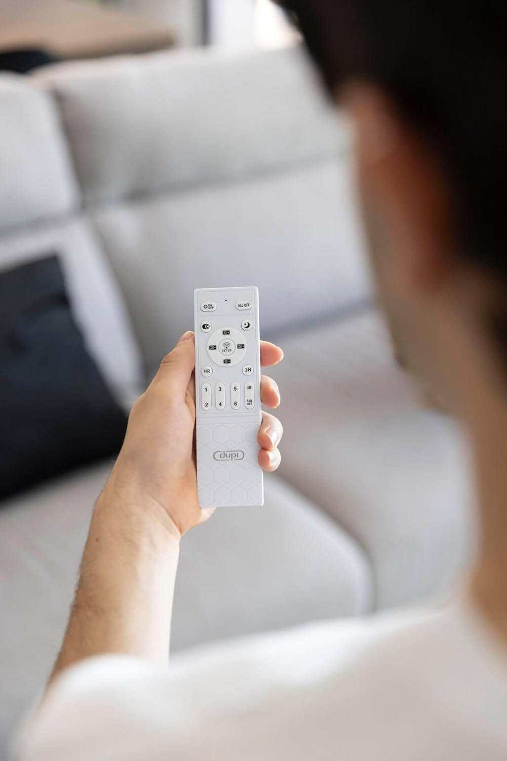 Una mano sostiene un mando a distancia blanco con botones y números.