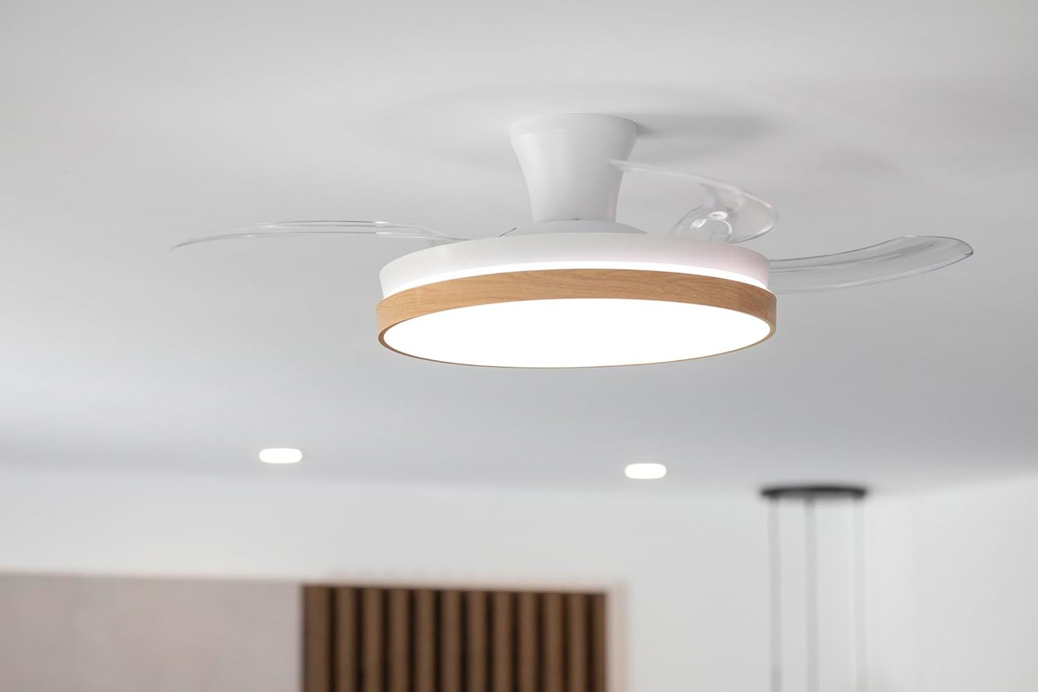 Ventilador de techo moderno con luz y borde de madera en techo blanco.
