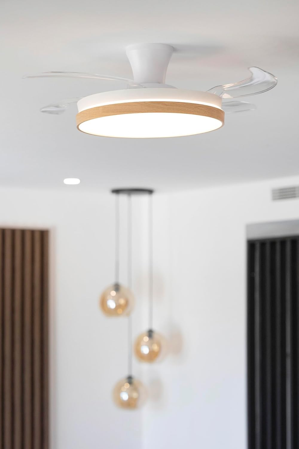 Ventilador de techo con luz LED y borde de madera, luces colgantes al fondo.