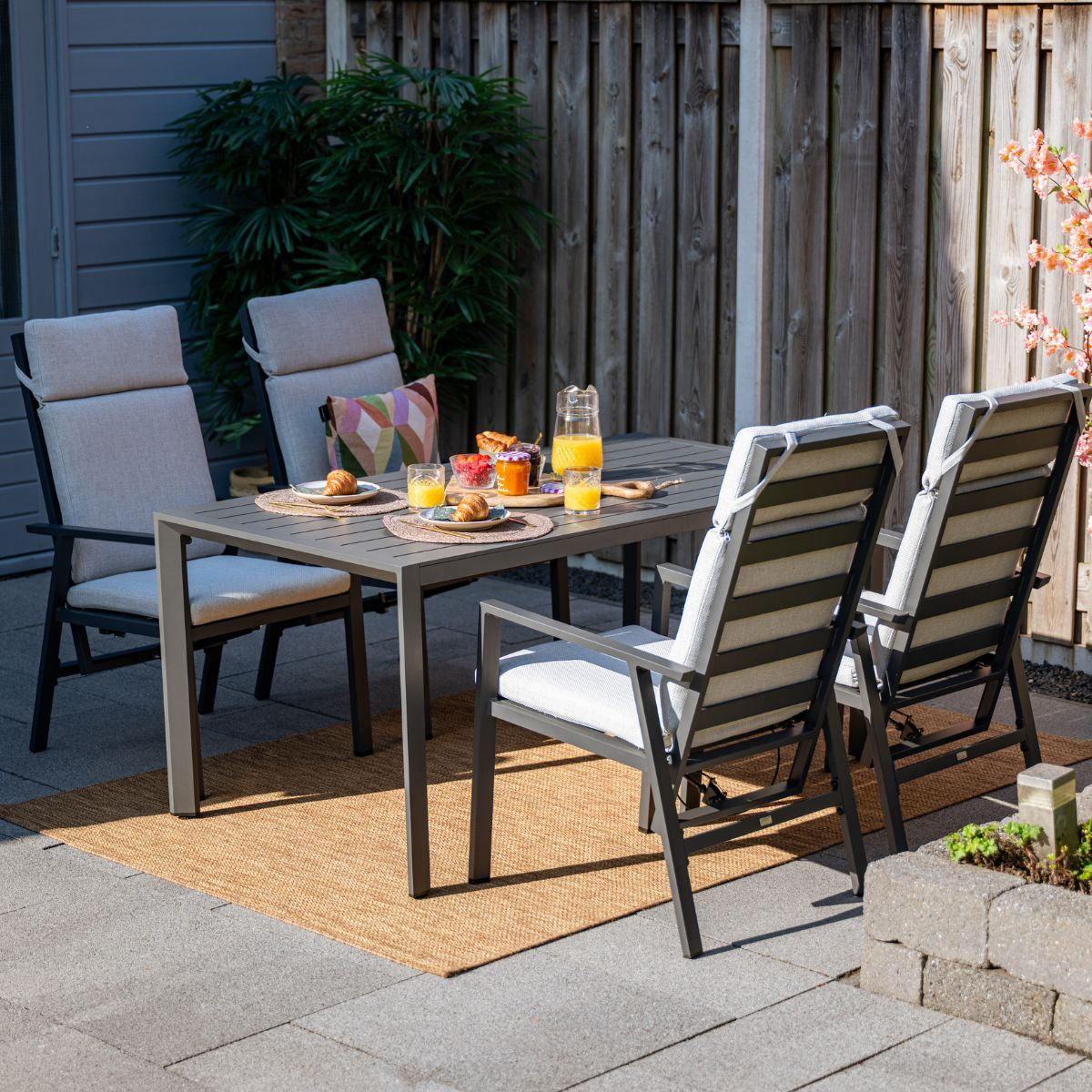 Een tuintafel gedekt voor ontbijt met croissants, jam en sinaasappelsap.