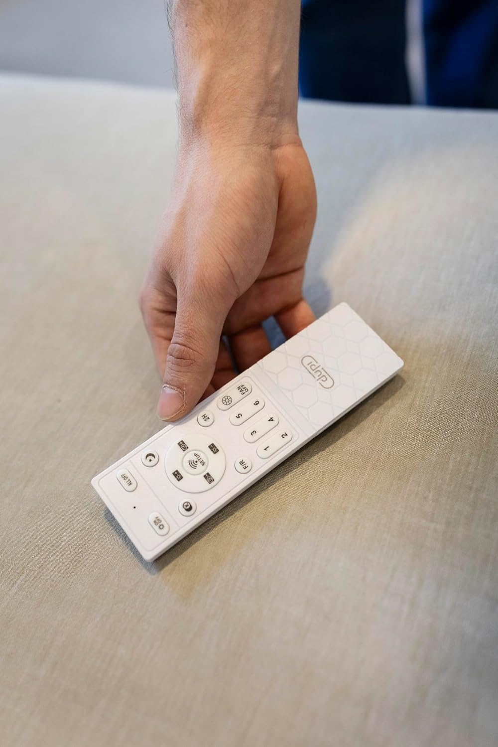 Una mano sostiene un mando a distancia blanco con botones y un diseño.