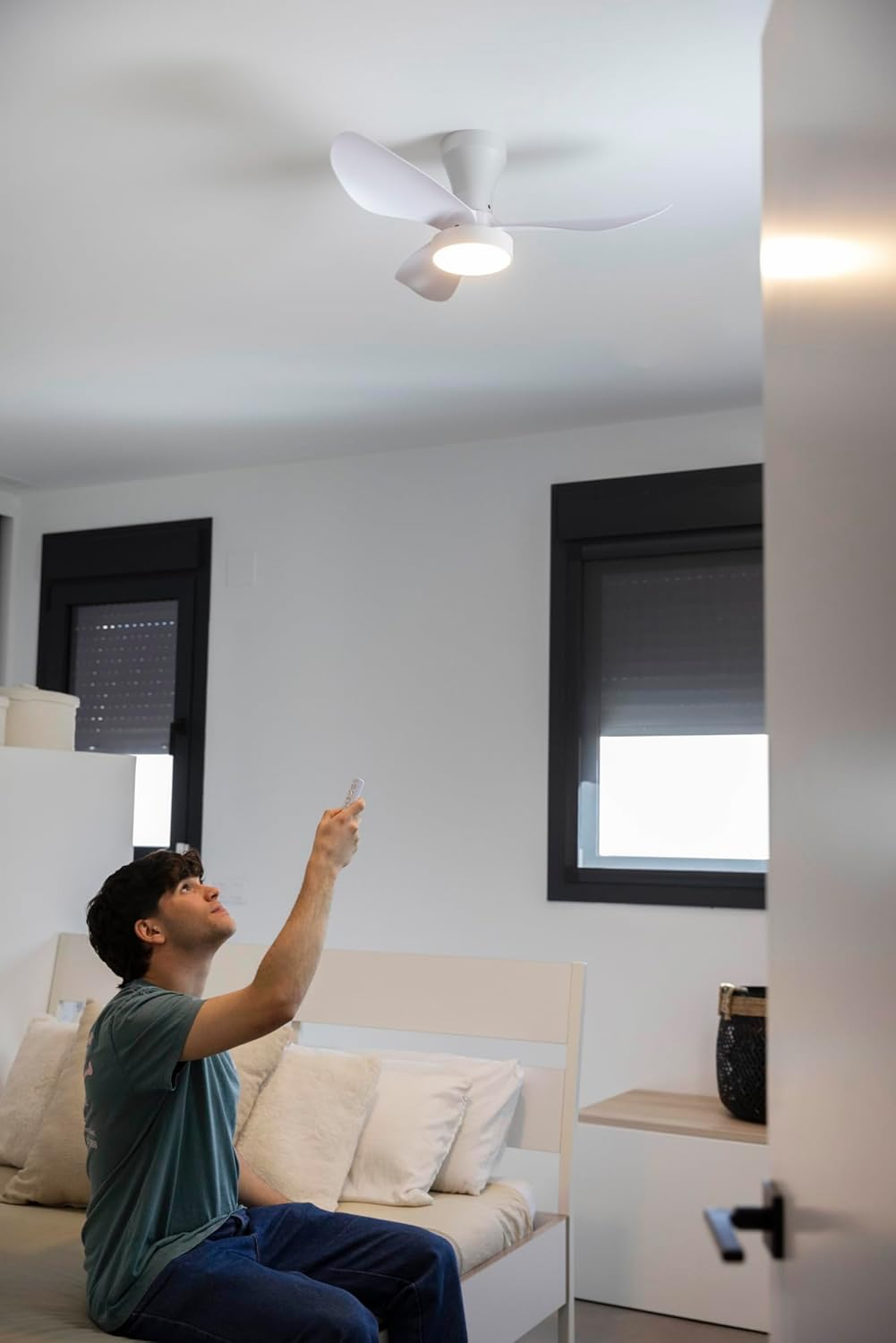 Hombre operando un ventilador de techo con control remoto en un dormitorio.