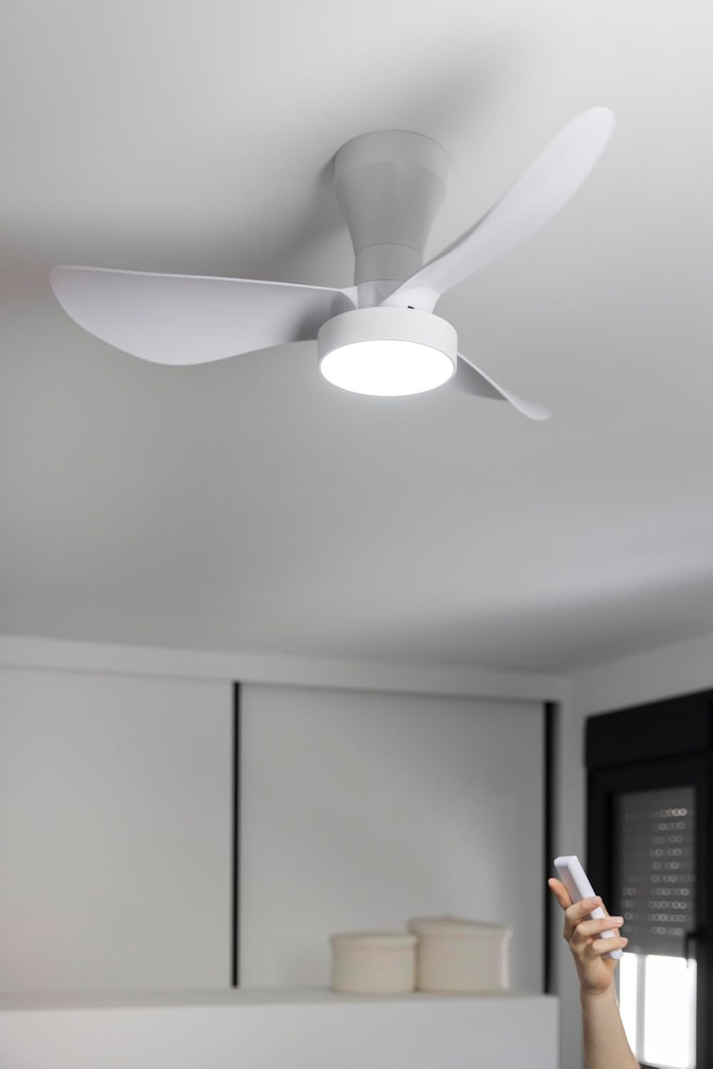 Un ventilador de techo blanco con luz y un mando a distancia en mano.
