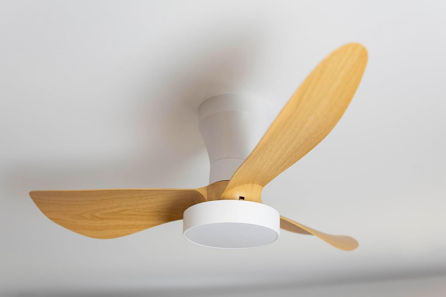 Un moderno ventilador de techo blanco con tres aspas de madera está montado en un techo blanco.