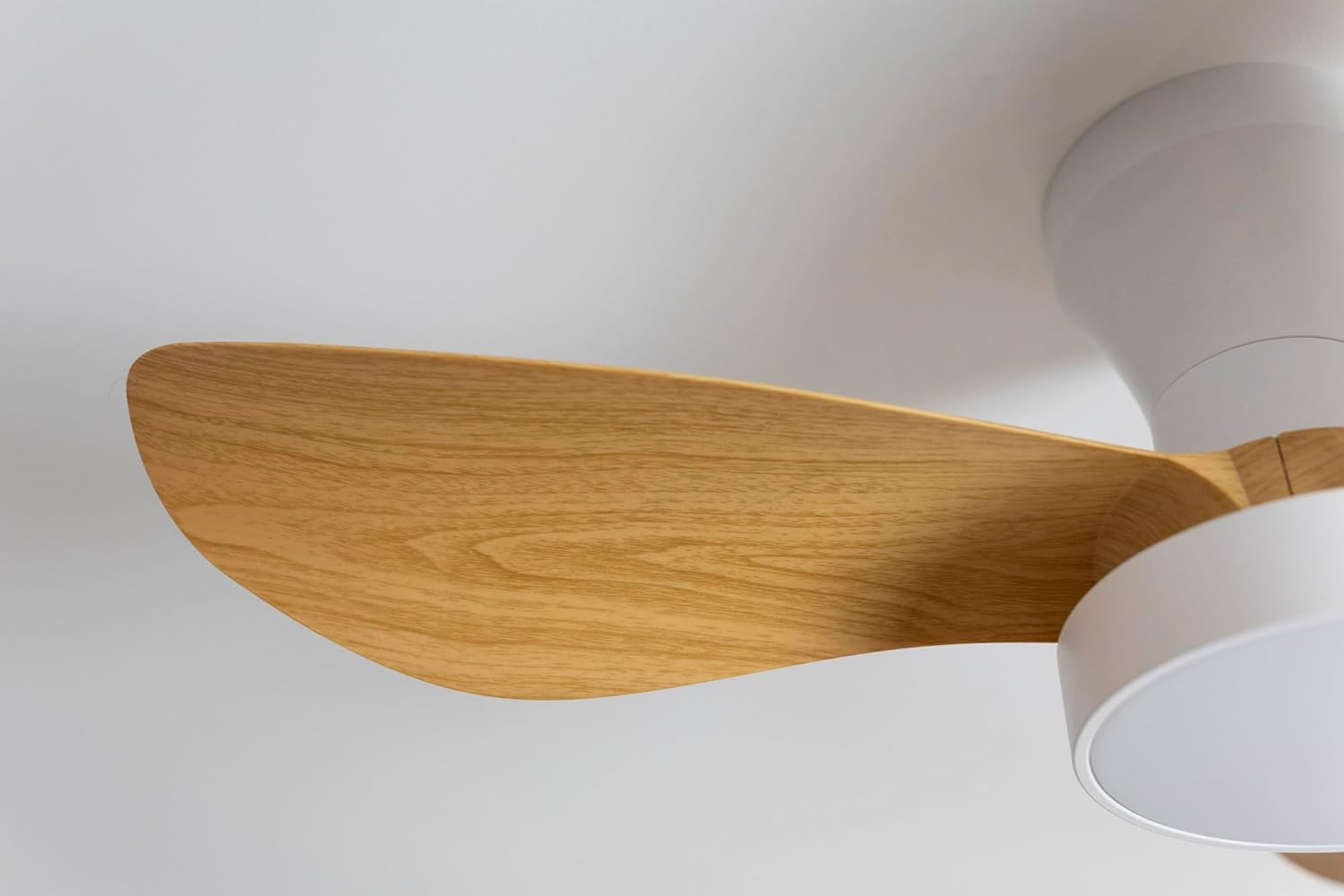 Una pala de ventilador de madera de un ventilador de techo con carcasa blanca.