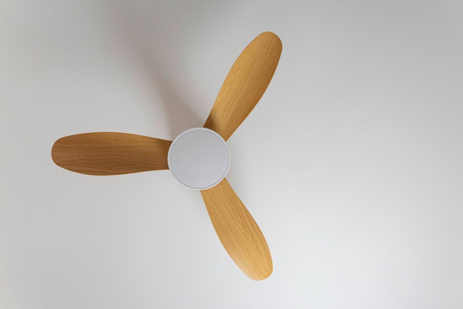 Un ventilador de techo con tres aspas de madera y un centro blanco redondo.