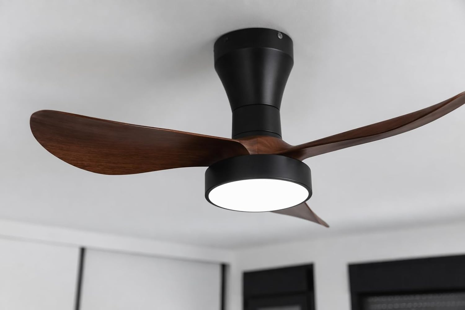 Un ventilador de techo moderno con aspas de madera oscura y soporte negro.
