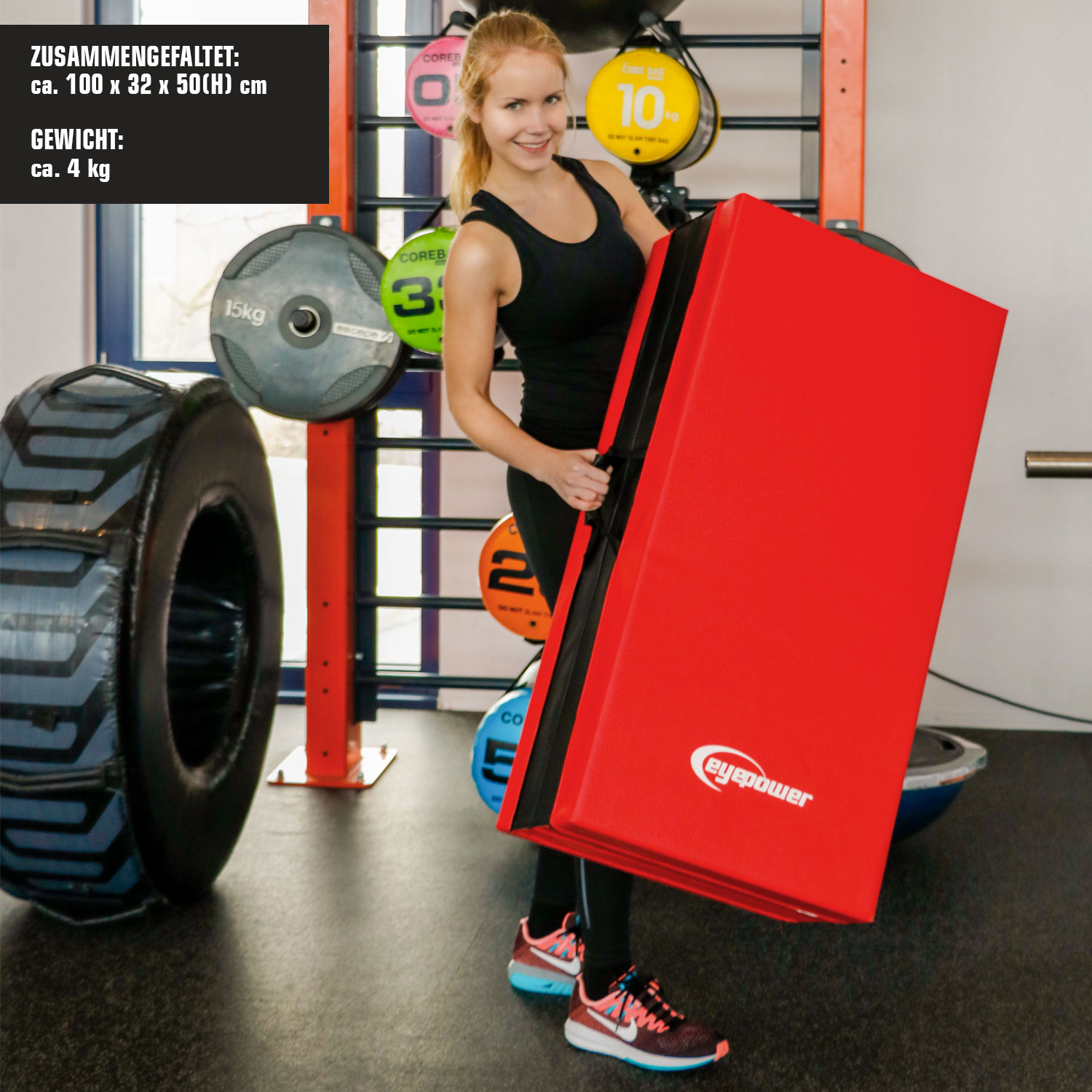 Eine Frau hält eine große, rote Fitnessmatte in einem Fitnessstudio. Links ist ein großes Rad zu sehen.