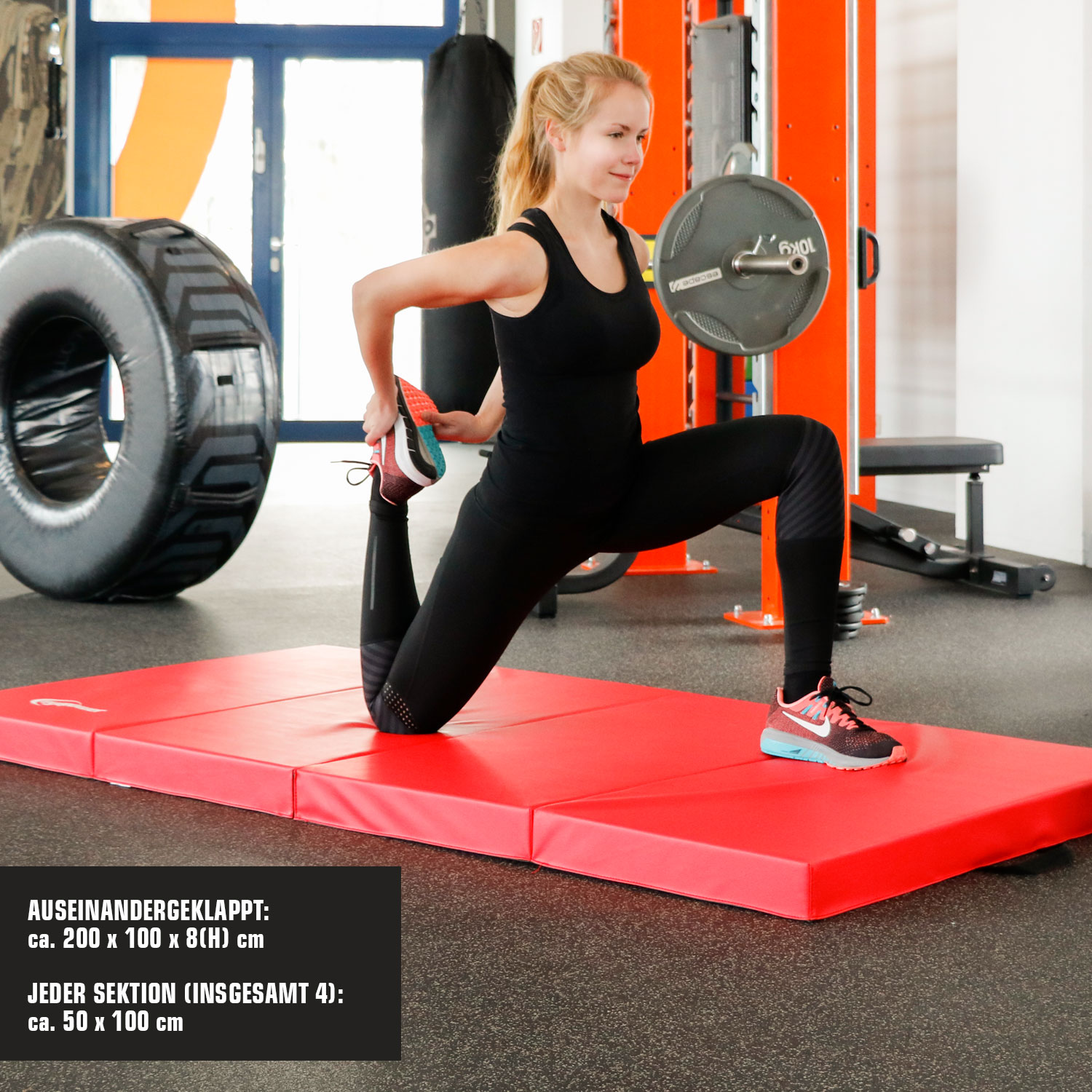 Eine Frau dehnt sich auf einer roten Matte in einem Fitnessstudio mit Gewichten und Reifen.