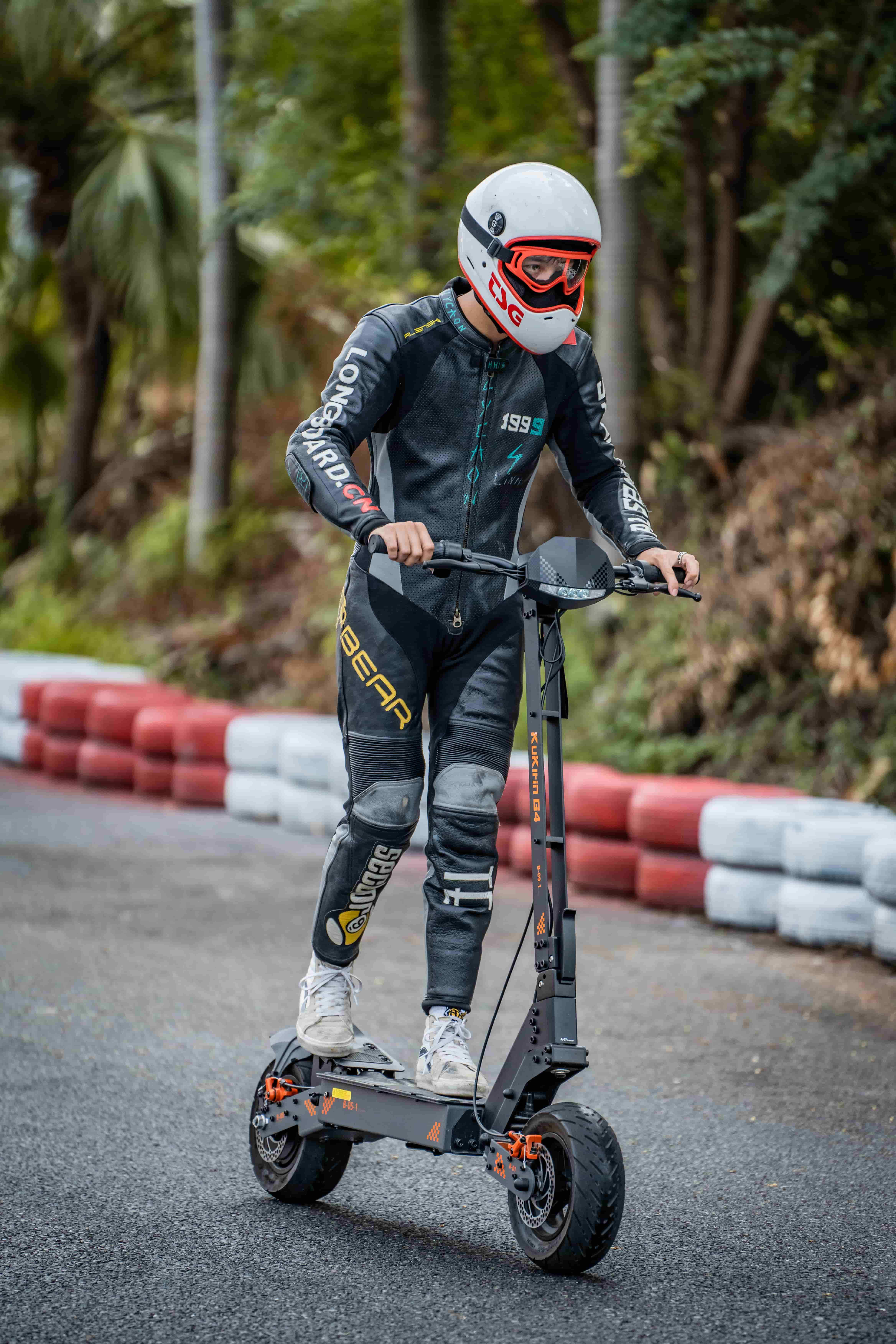 Cavaliere in tuta di pelle su scooter elettrico su pista con barriere rosse/bianche.