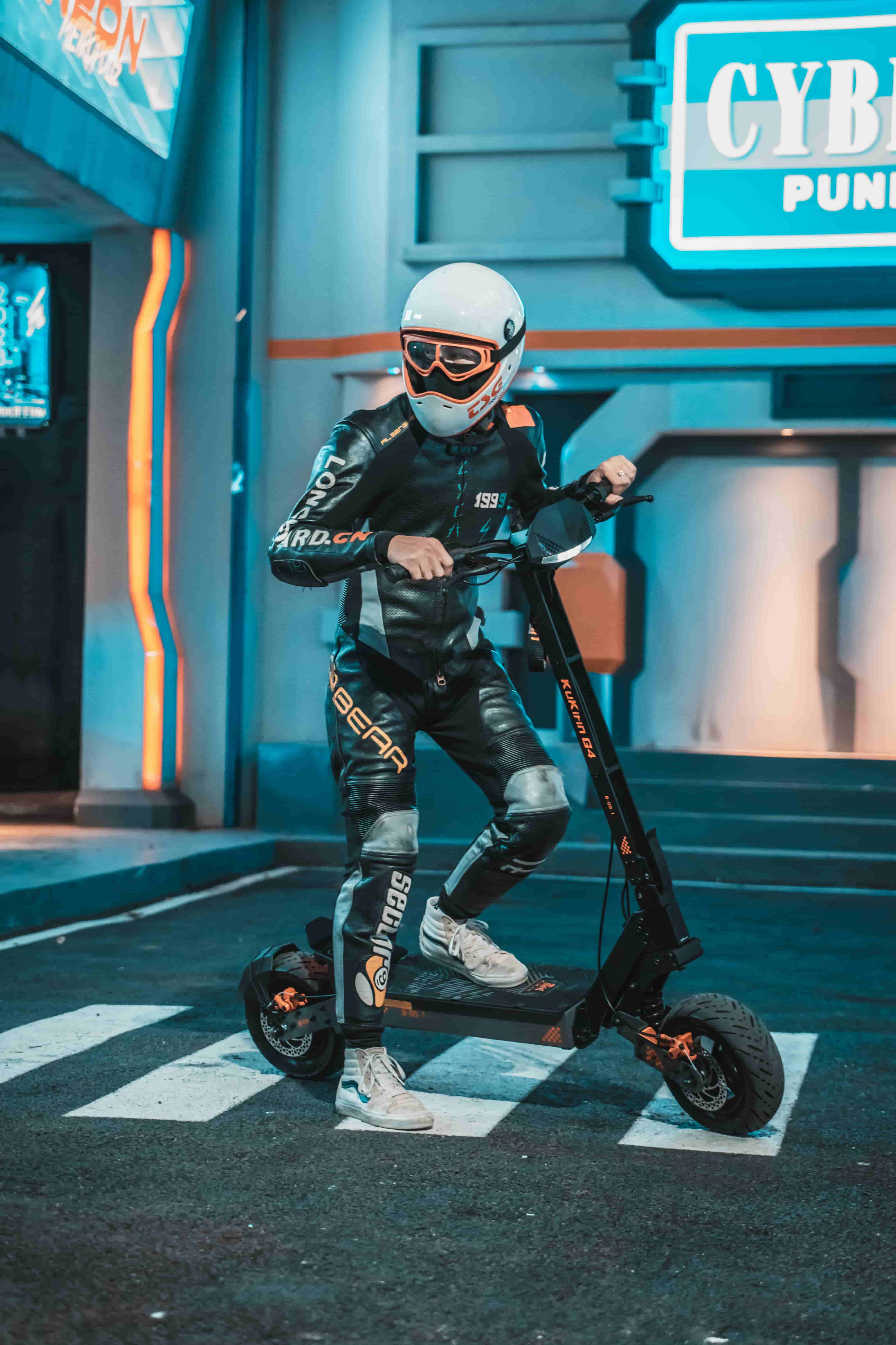 Una persona in tuta da corsa in pelle e casco guida un monopattino elettrico su un attraversamento pedonale.