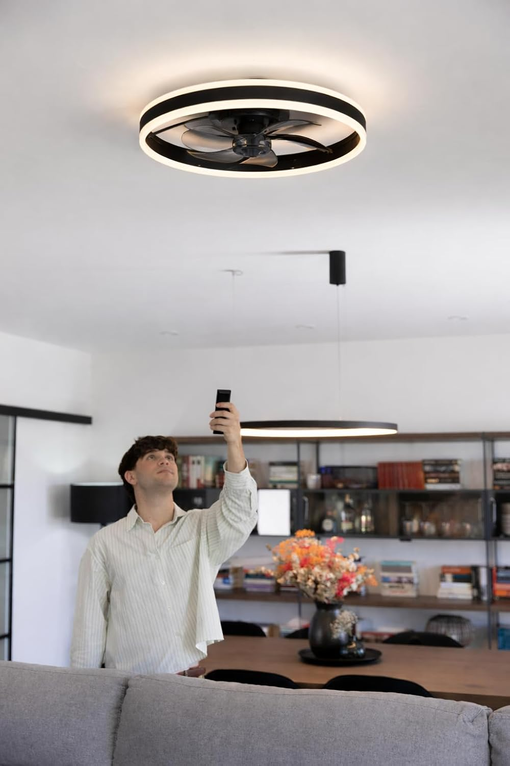 Un hombre sostiene un control remoto y mira un ventilador de techo con luz.