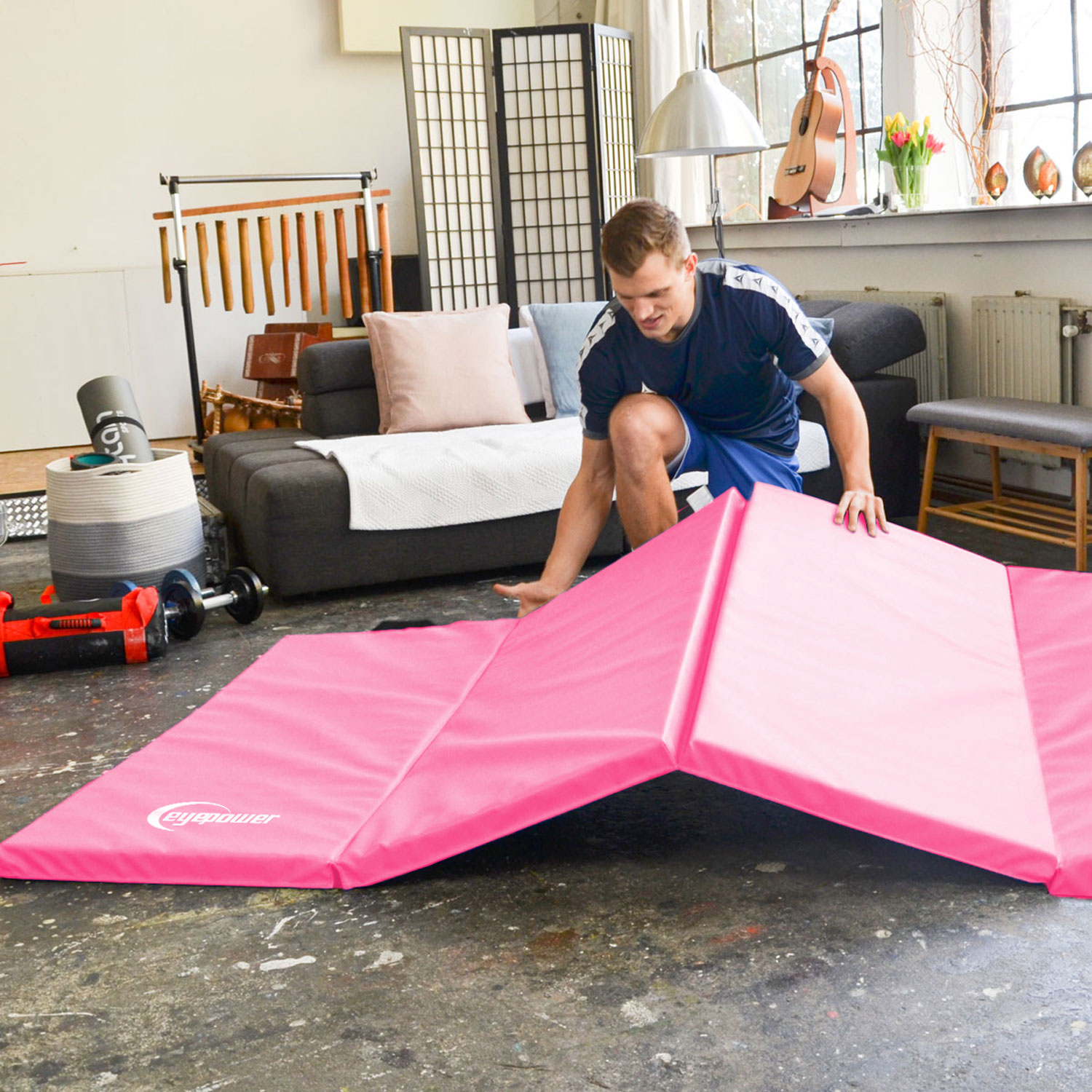 Ein Mann breitet eine rosa Gymnastikmatte in einem Wohnzimmer aus.