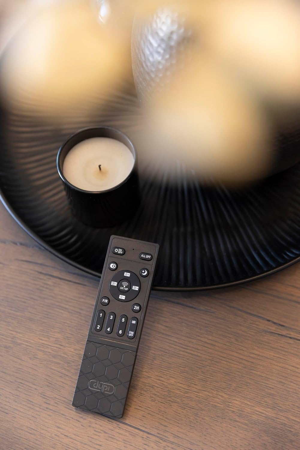Un control remoto negro con botones está sobre una mesa de madera junto a una vela blanca en un soporte negro.