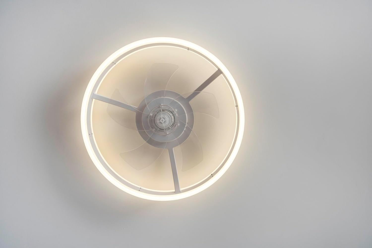 Un ventilador de techo moderno con luz LED circular y tres aspas transparentes, sobre un techo blanco.