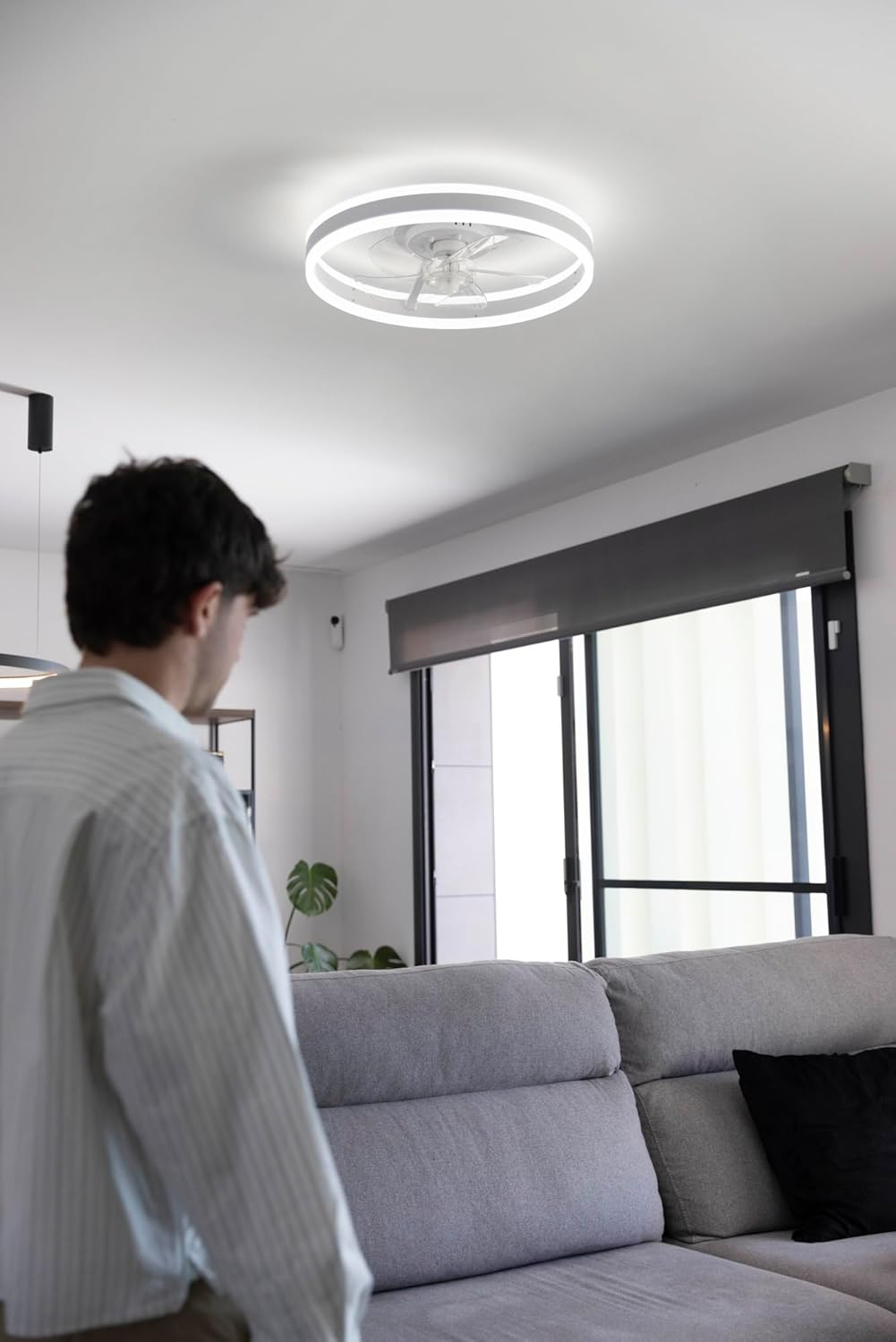 Hombre delante de sofá; ventilador de techo con luz encima.