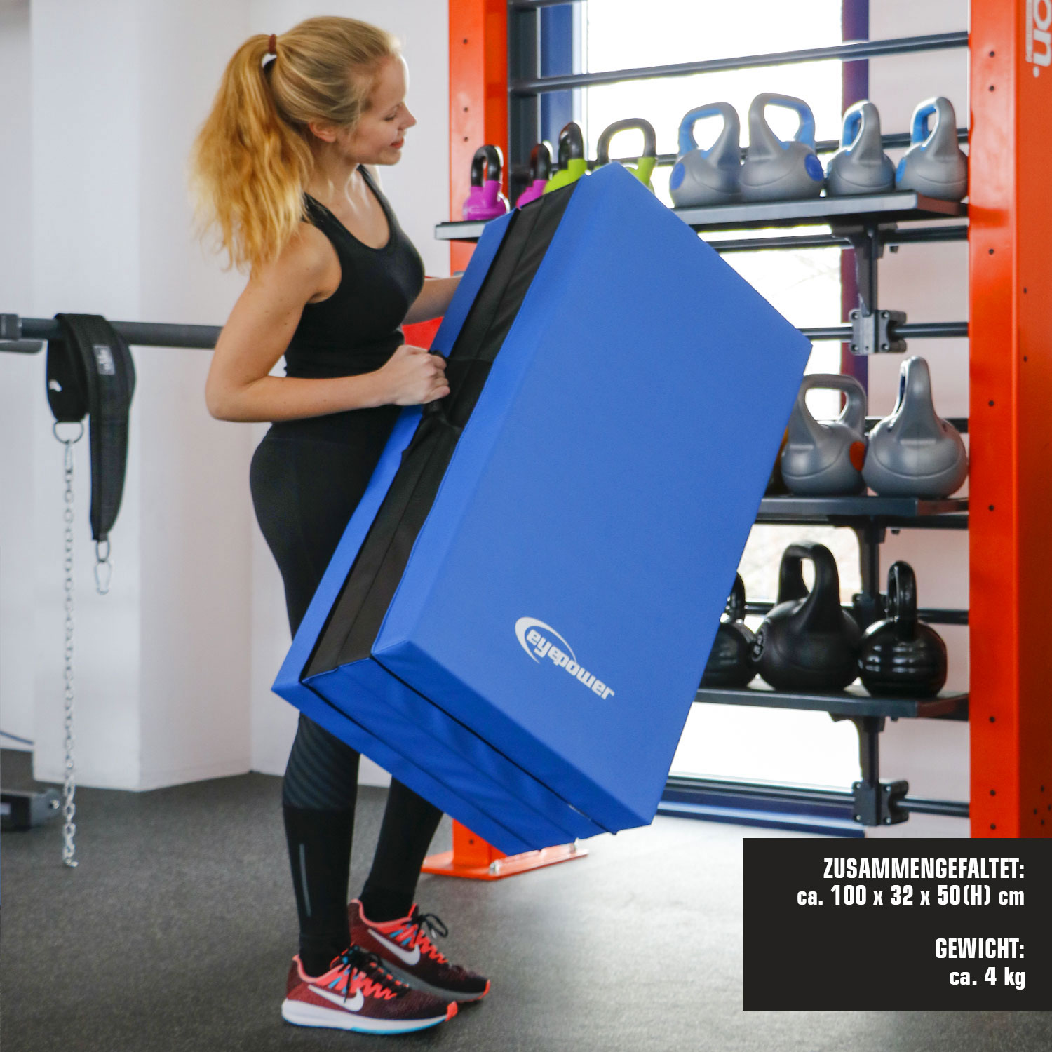 Eine Frau in Schwarz trägt eine blaue Matte in einem Fitnessstudio mit Kettlebells.