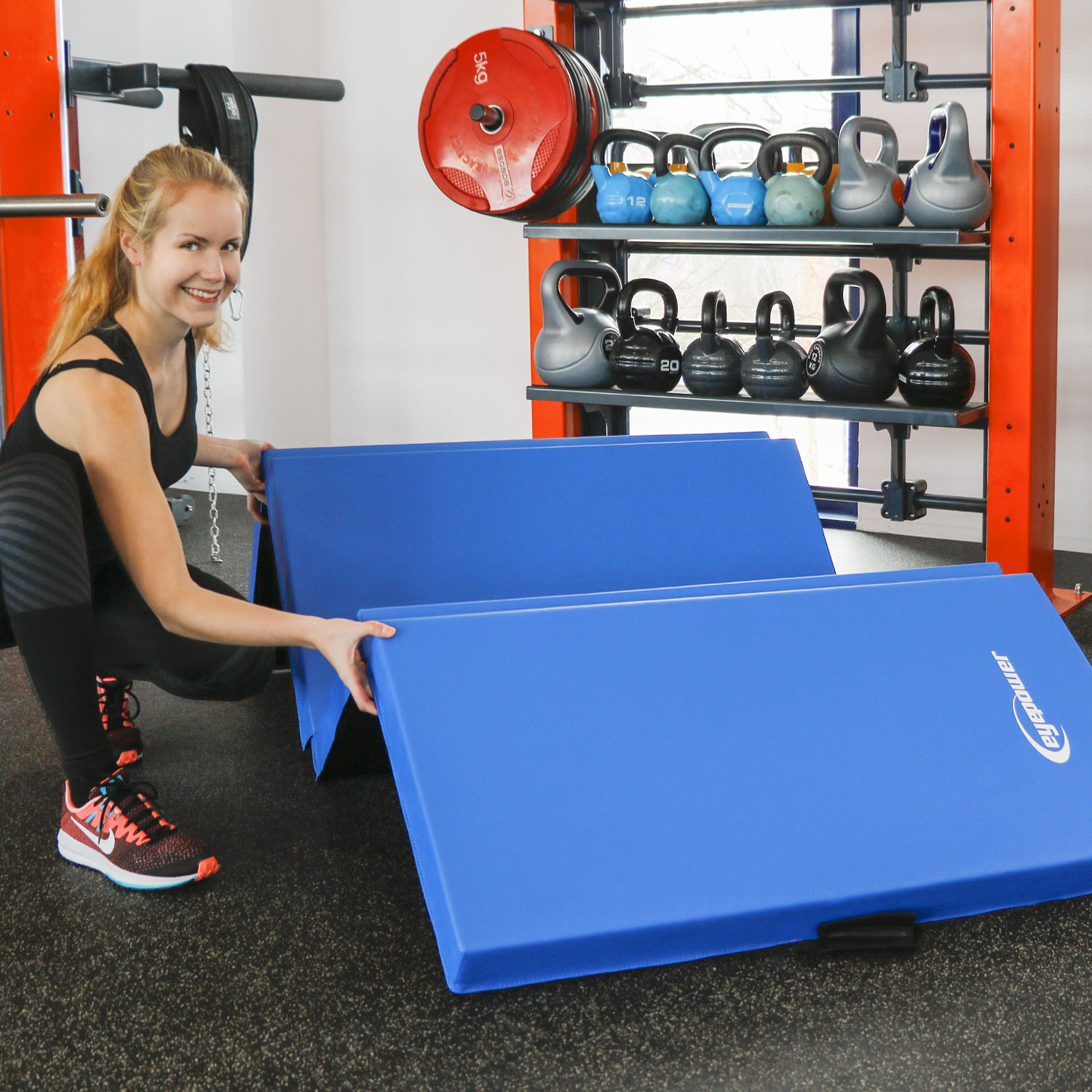 Eine Frau richtet blaue Gymnastikmatten in einem Fitnessstudio ein.