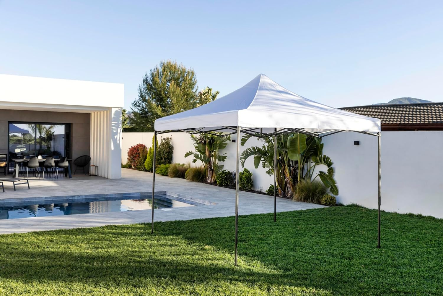 Una carpa blanca junto a una piscina y una casa moderna con jardín.