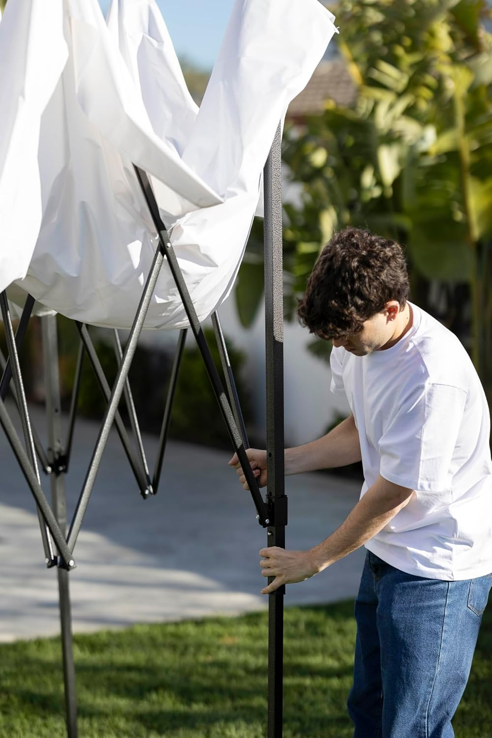 Un hombre con camiseta blanca ajusta la estructura de una carpa negra. Lona blanca encima.