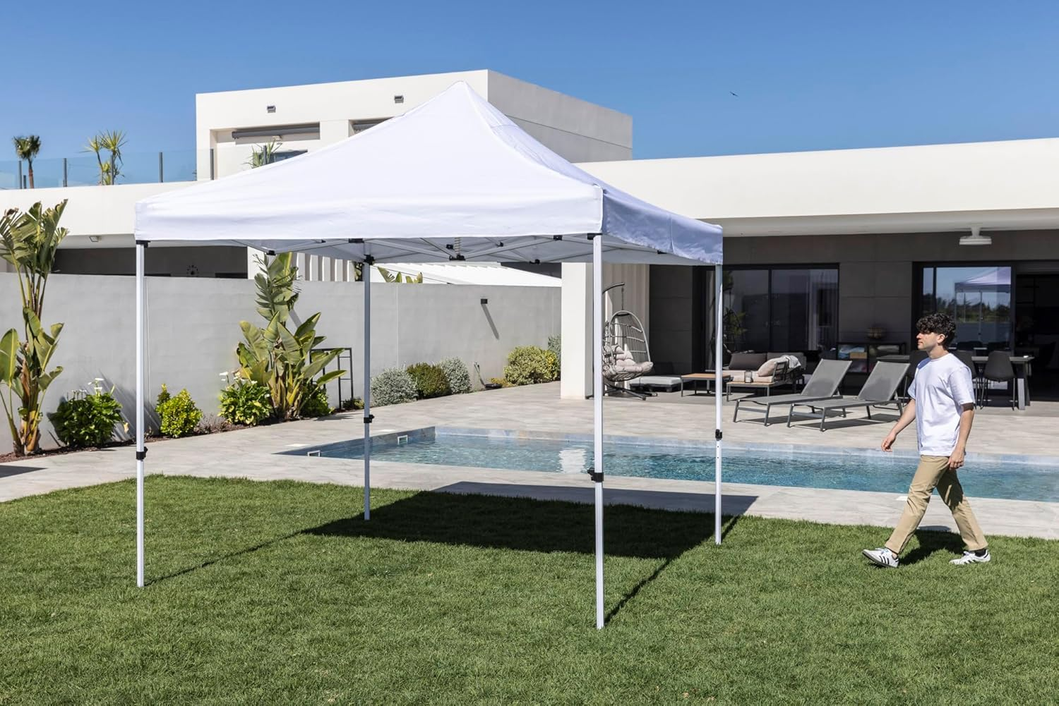 Un hombre pasa junto a una piscina bajo un toldo blanco en un patio trasero.