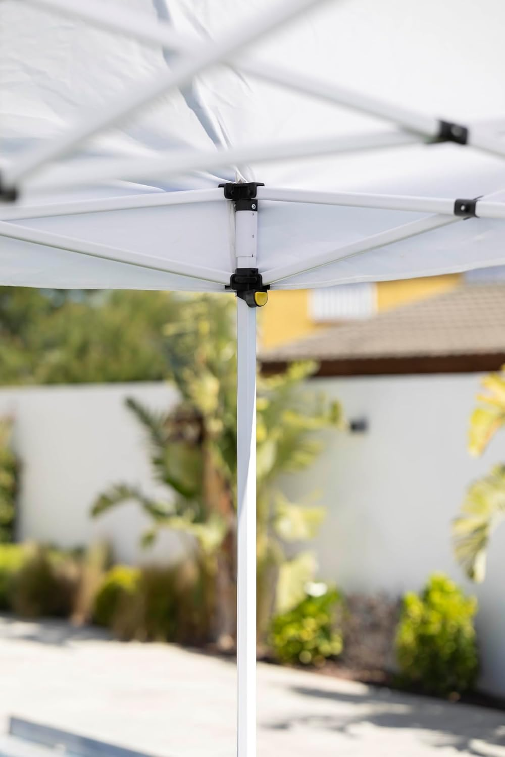Estructura de carpa blanca con tela, fondo de árboles y casa.