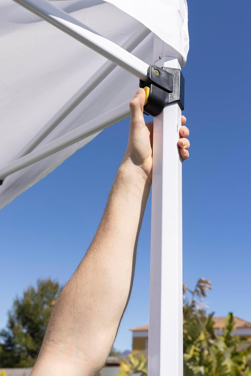 Una mano presiona un botón amarillo en una estructura de carpa blanca bajo cielo azul.