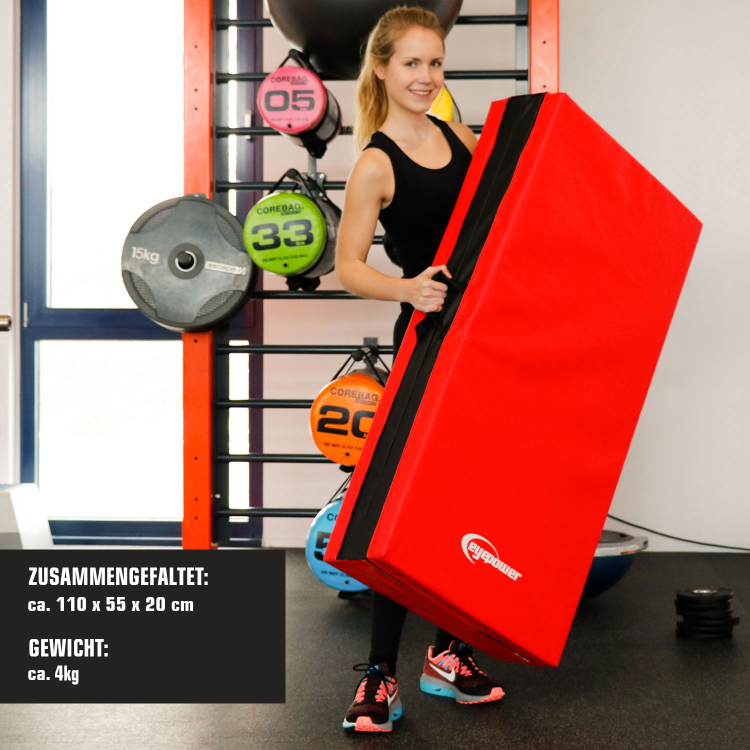 Eine Frau hält ein großes rotes Trainingskissen mit schwarzem Rand in einem Fitnessstudio.