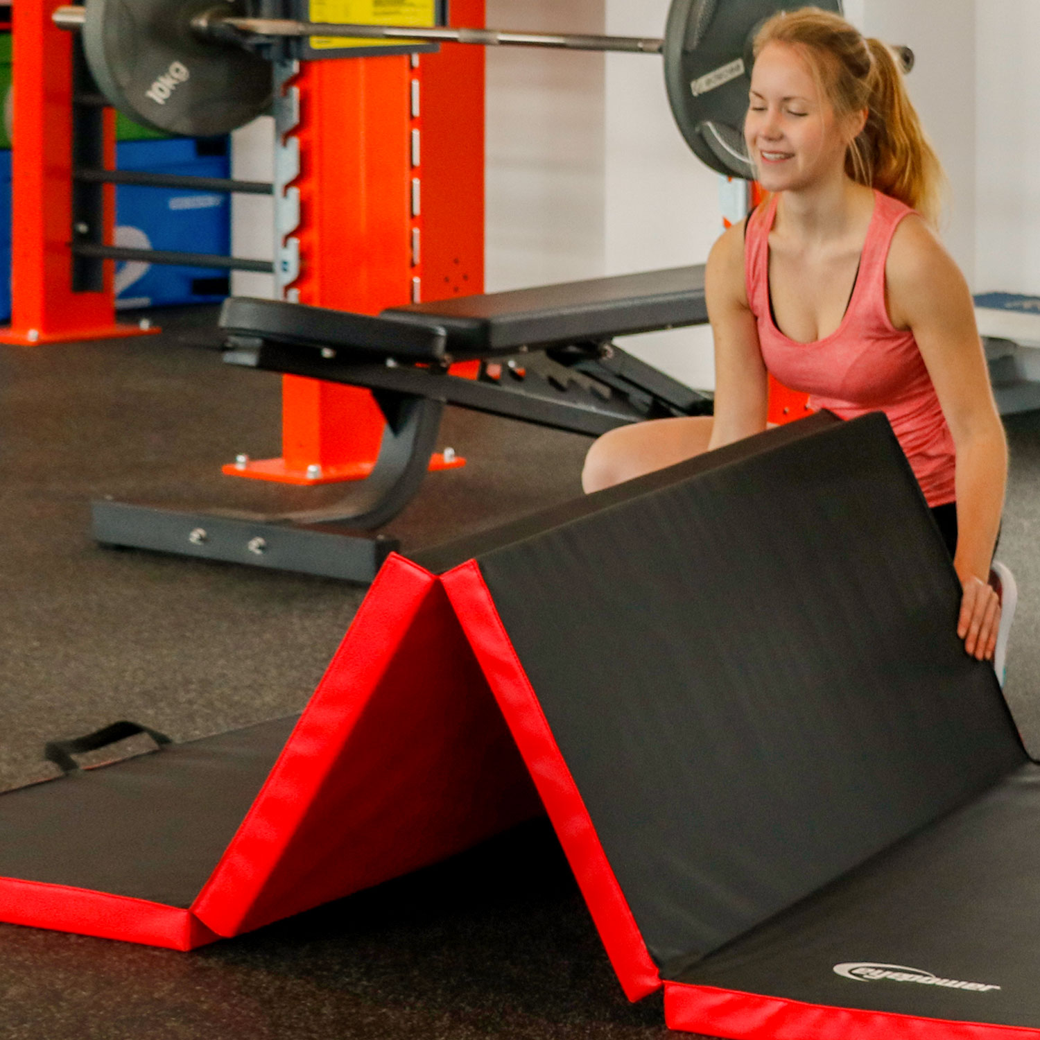 Eine Frau im Fitnessstudio stellt eine schwarze Matte mit rotem Rand auf.