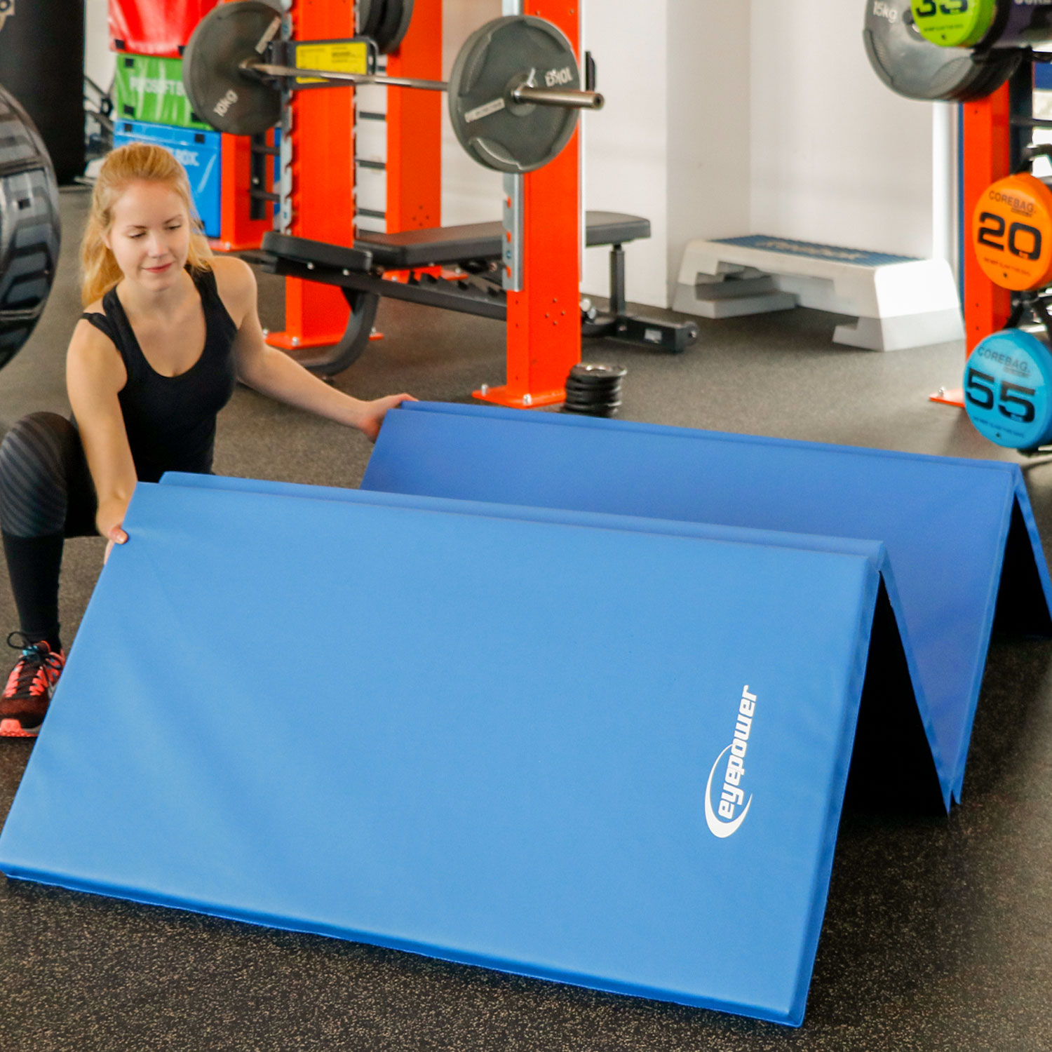 Eine Frau legt blaue Matten in einem Fitnessstudio aus.