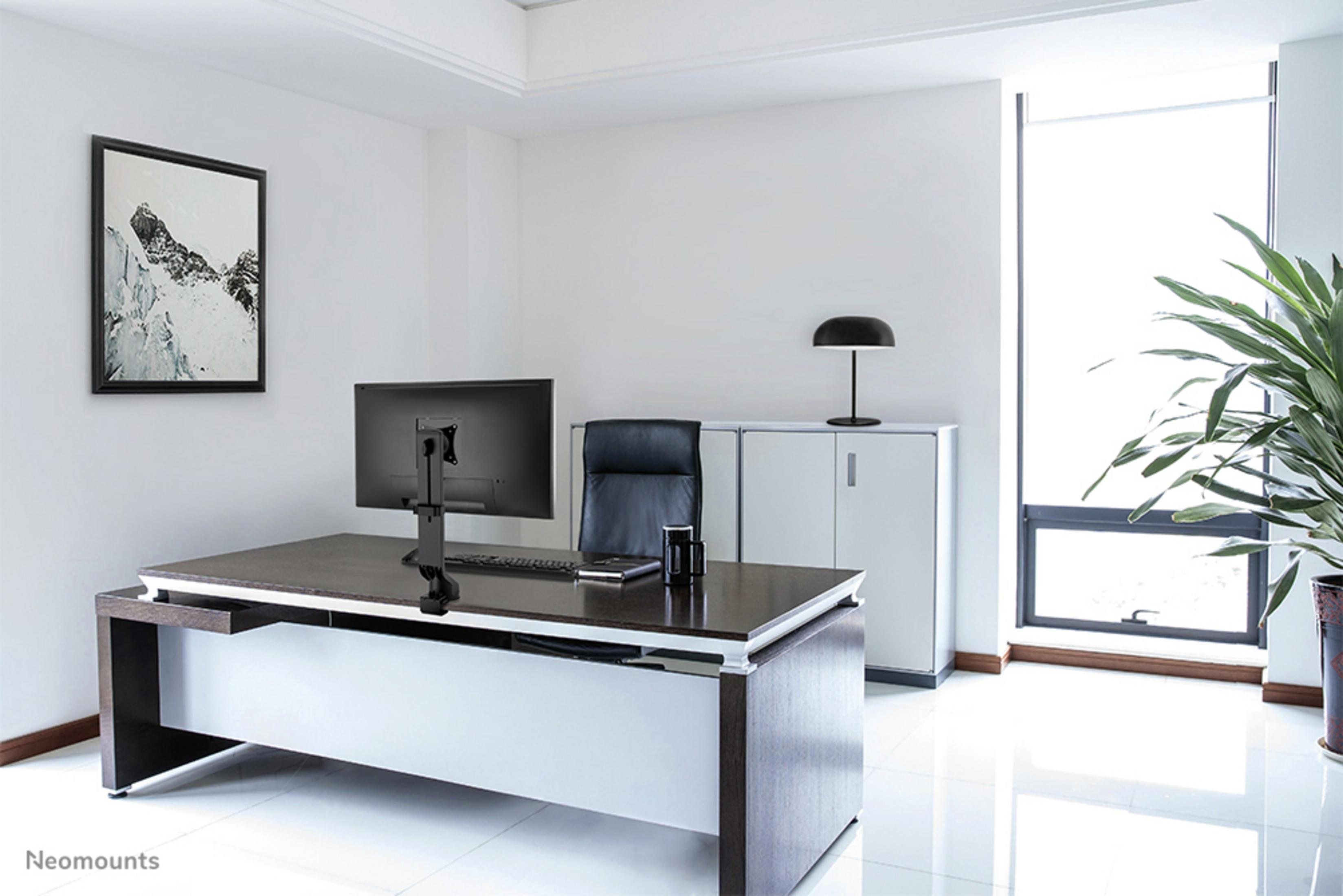Een modern kantoor met bureau, monitor, stoel en een ingelijst schilderij.