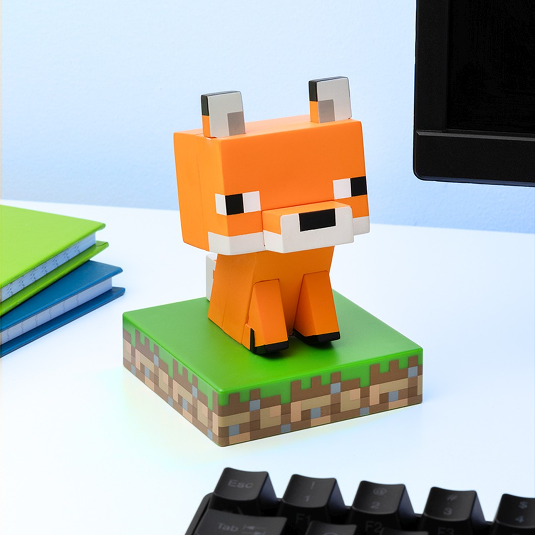 Ein Minecraft-Fuchs-Spielzeug sitzt auf einem Grasblock neben Büchern und einer Tastatur.