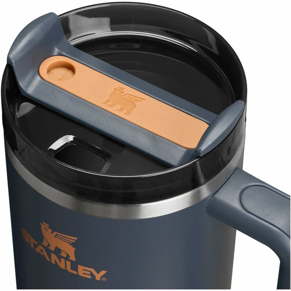 Dunkelgrauer Stanley Becher mit orangefarbenem Logo und Griff. Der Deckel hat einen Schieber.