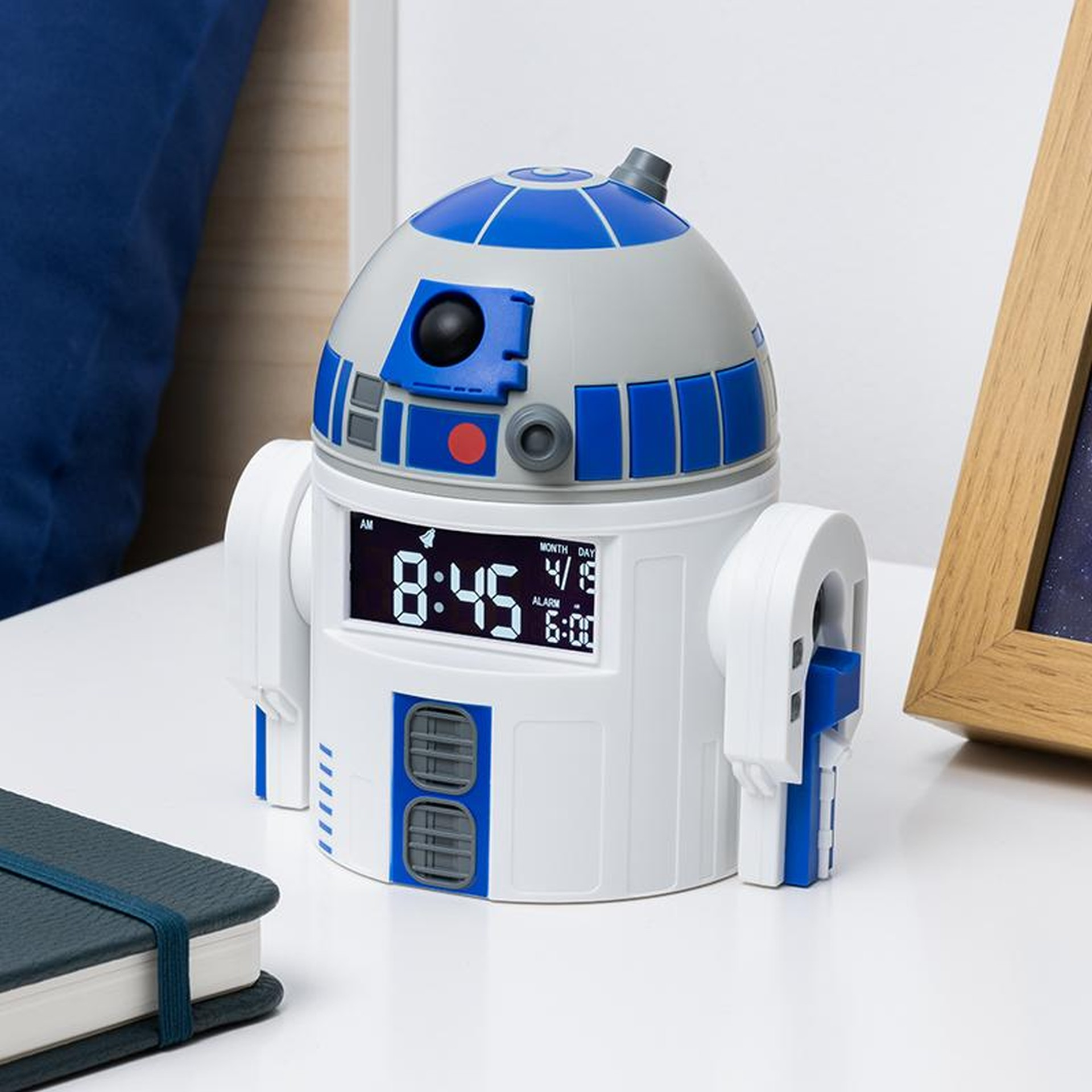 Budzik R2-D2 stoi na białym stole obok notatnika i ramki na zdjęcia.