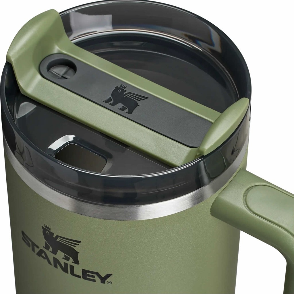 Primer plano de una taza verde Stanley con tapa gris y logo de oso alado.