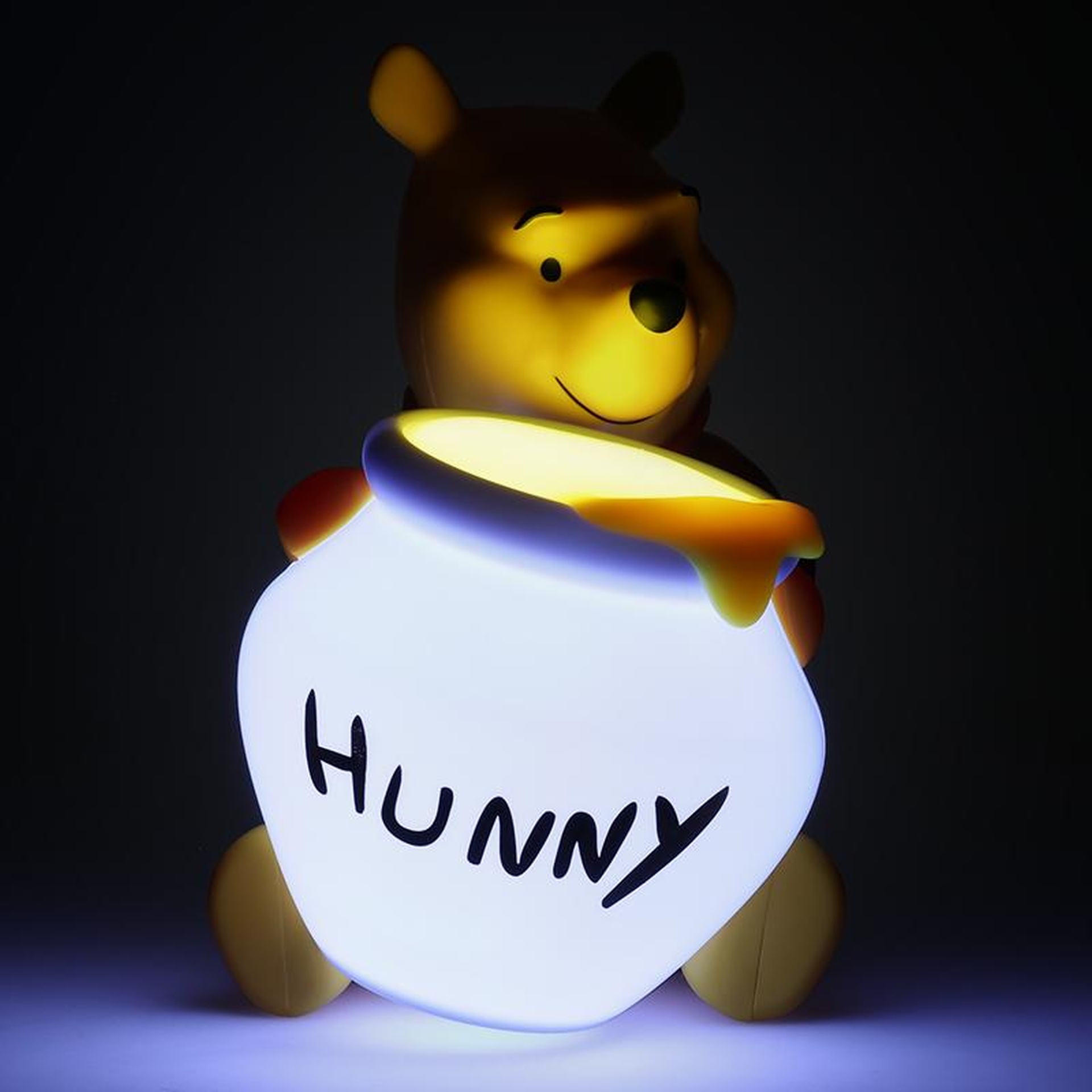 Świecąca lampka Kubusia Puchatka trzyma słoik z napisem 'Hunny'.