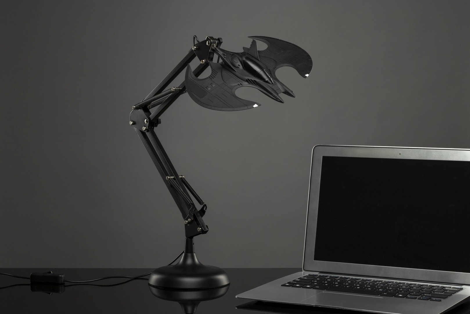 Ein schwarzer Schwanenhals-Schreibtischlampenarm mit einer Fledermaus-inspirierten Lampe und einem Laptop.