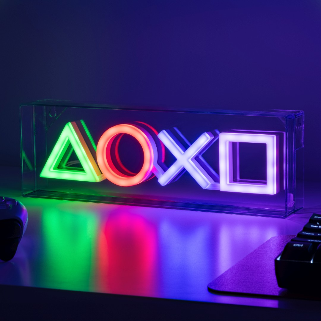 Podświetlone symbole PlayStation (trójkąt, koło, X, kwadrat) w pudełku na biurku.