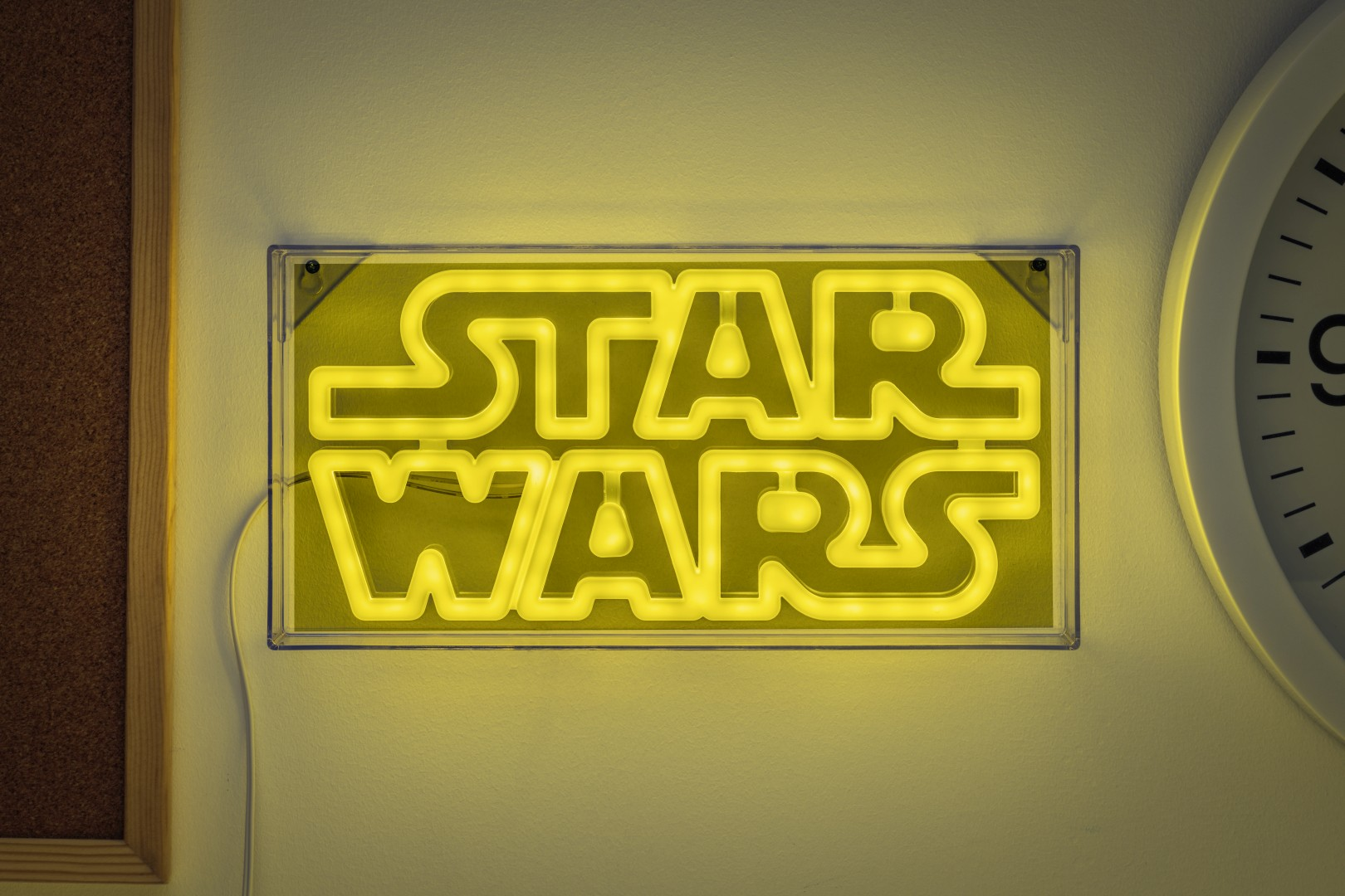 Żółty neonowy napis "STAR WARS" świeci na ścianie obok zegara.