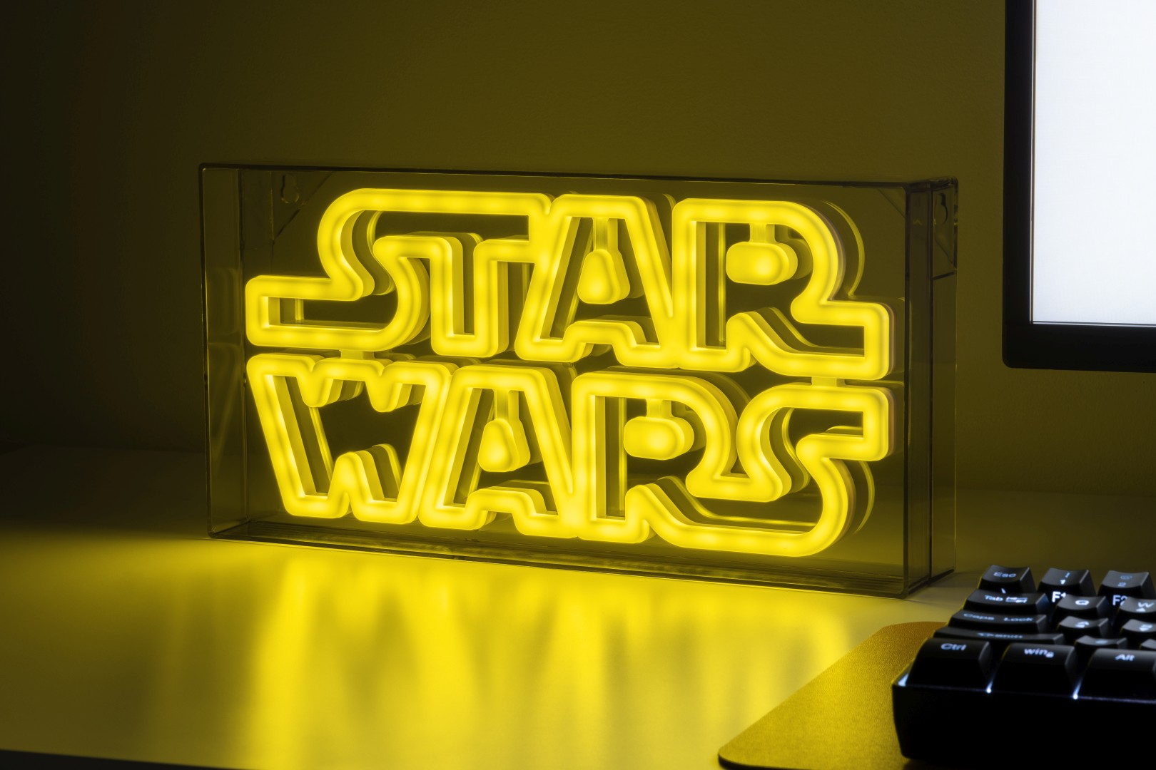 Żółty neonowy znak Star Wars w przezroczystej obudowie na biurku z klawiaturą.