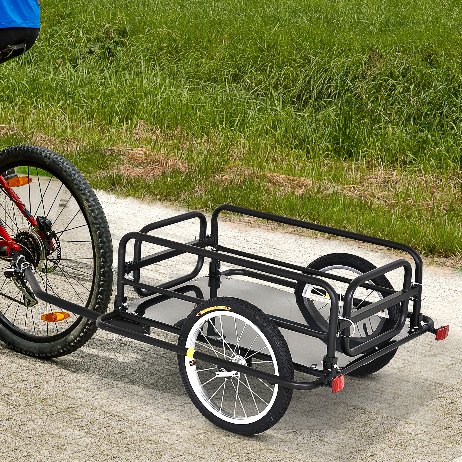 Un remolque de bicicleta de dos ruedas está acoplado a una bicicleta. Hierba verde al fondo.
