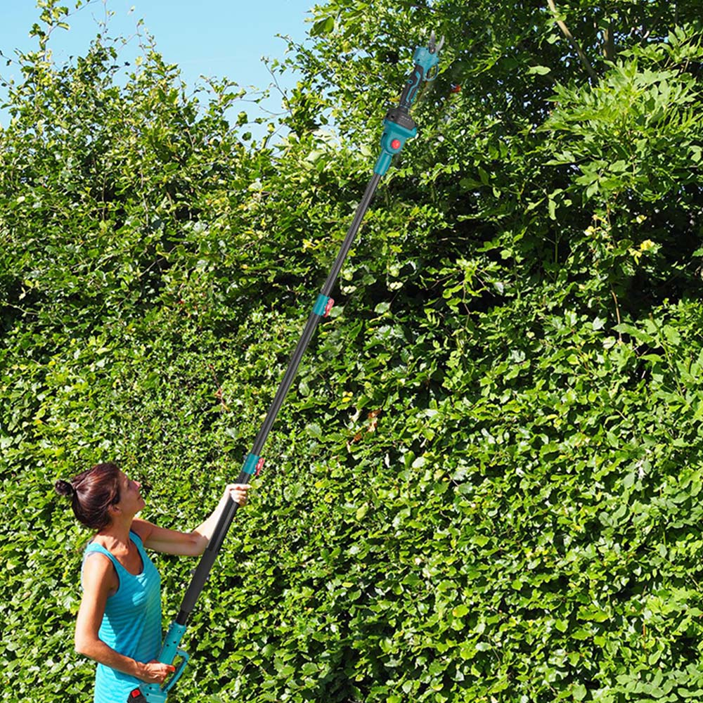 Eine Frau in einem blauen Tanktop schneidet eine hohe Hecke mit einer Langstiel-Astsäge unter klarem Himmel.