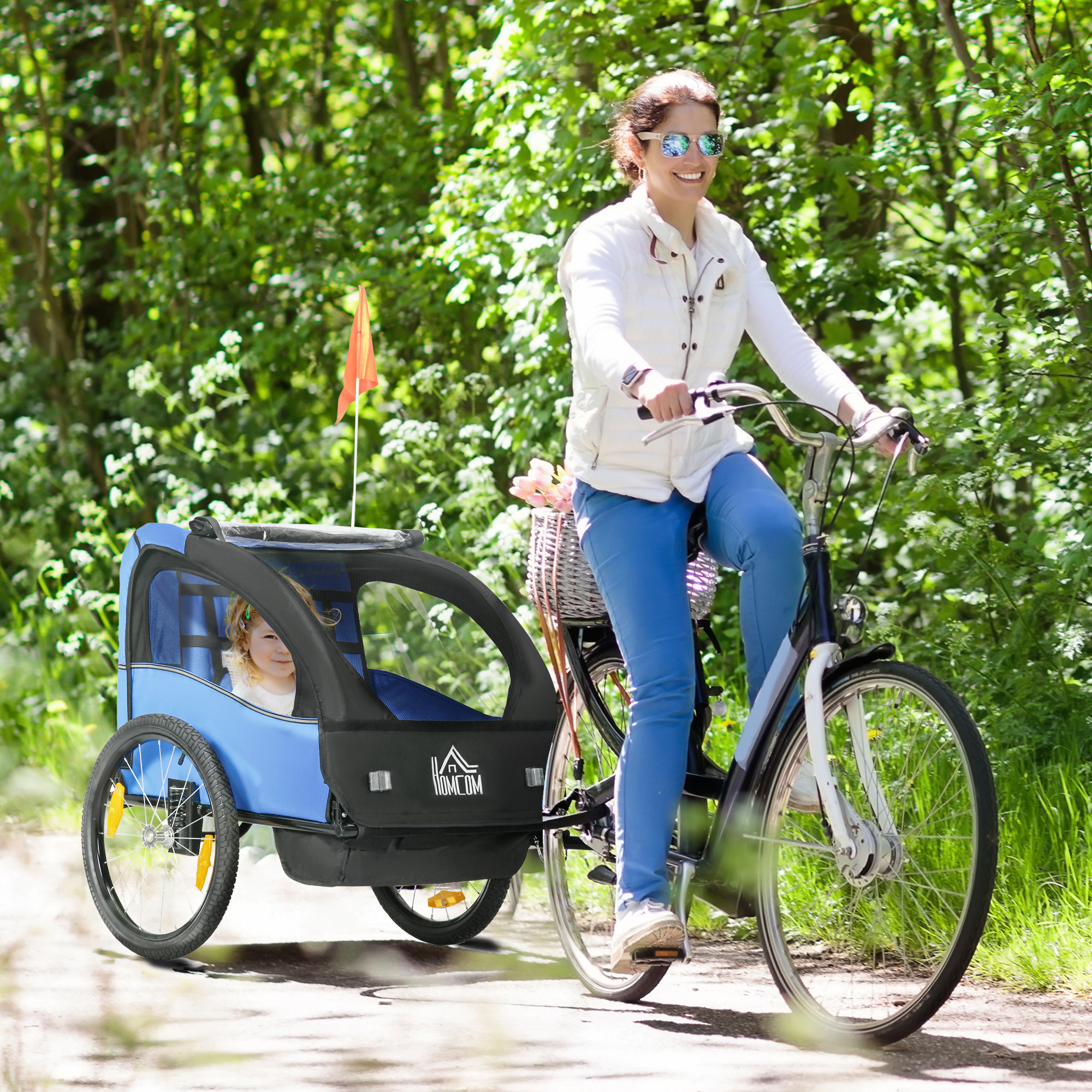 Una mujer monta en bicicleta con un remolque infantil azul en el bosque.