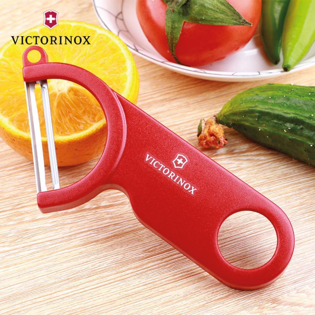 Kırmızı bir Victorinox soyucu, bir portakal dilimi ve sebzelerin yanında duruyor.