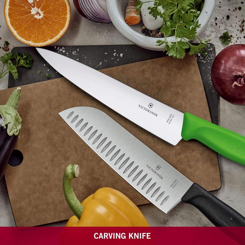 İki Victorinox bıçağı, biri yeşil saplı, diğeri siyah, sebzeli kesme tahtasında.