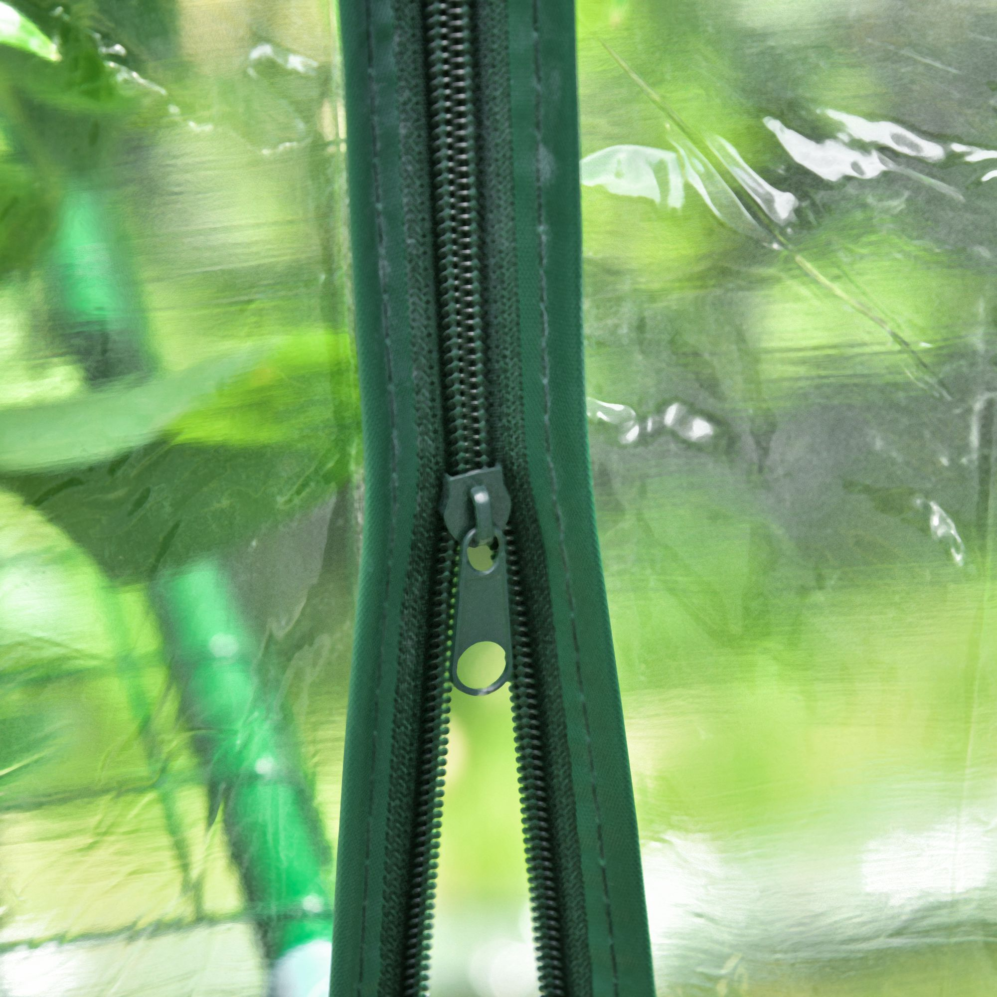 Una cremallera verde sobre una cubierta transparente con plantas al fondo.