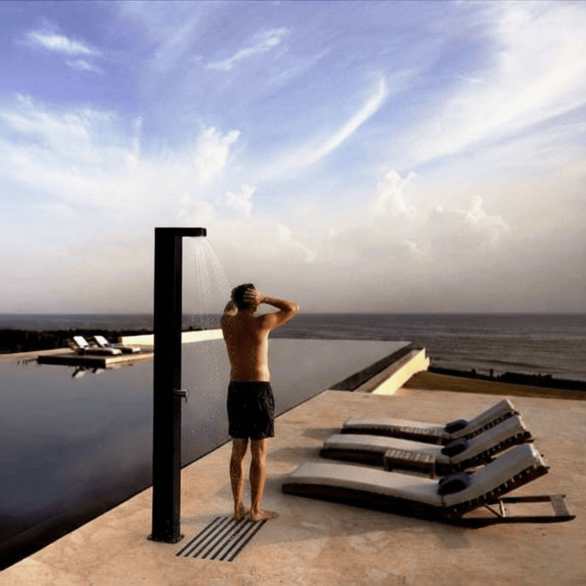 Un hombre se ducha al aire libre junto a una piscina infinita con vista al mar.