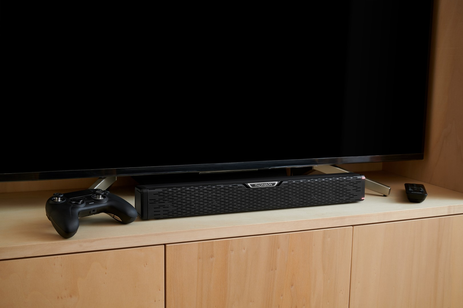 Czarny soundbar z pilotem i kontrolerem przed telewizorem.