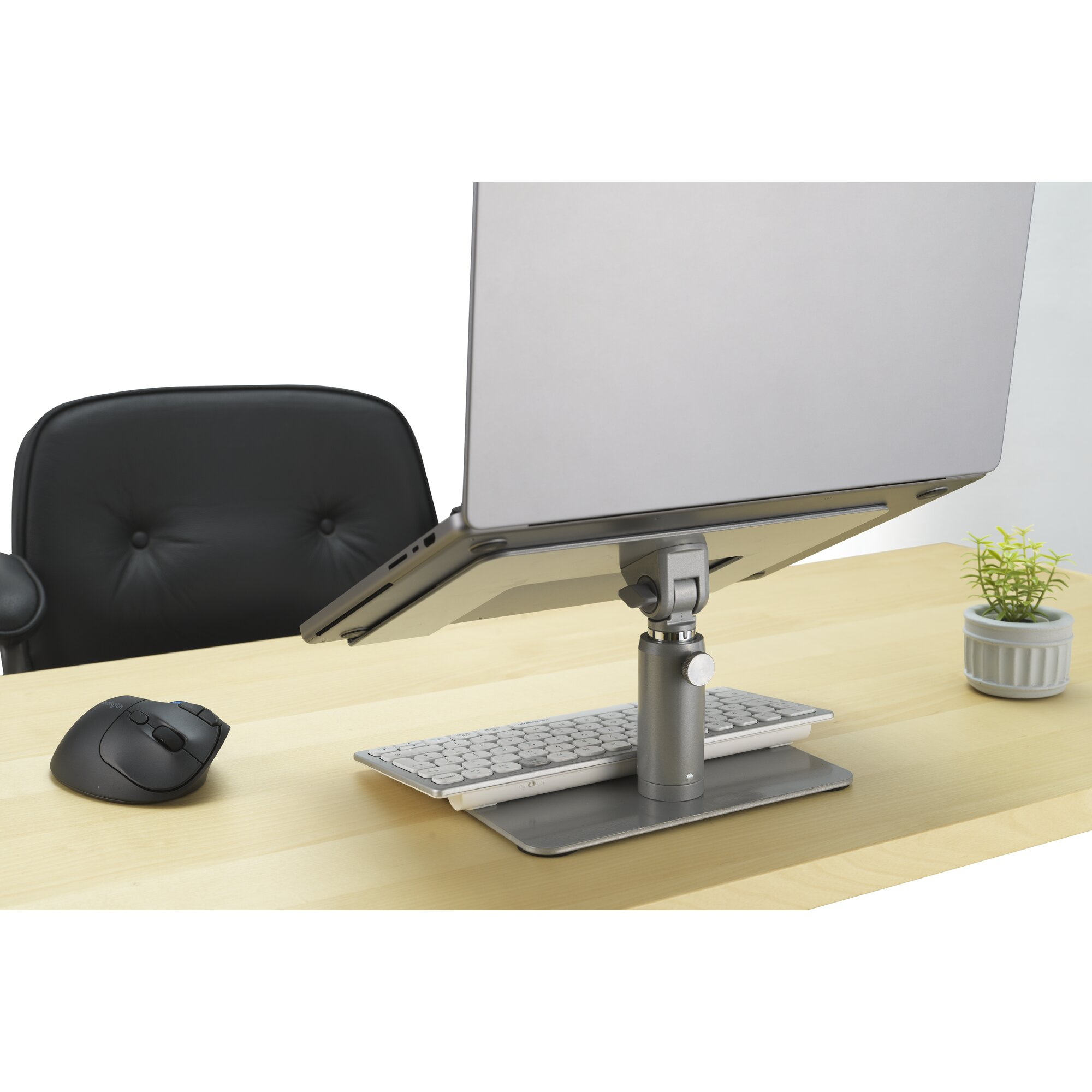 A laptop on a stand with a keyboard and mouse on a desk.